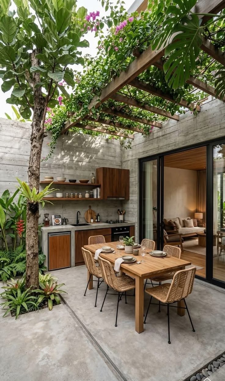 An outdoor kitchen and dining table under a planted pergola